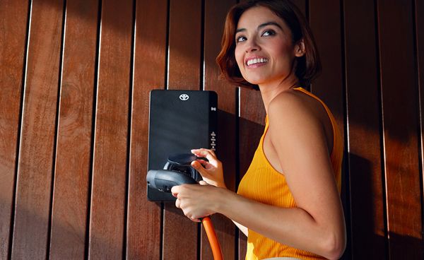 Kobieta stoi przy domowej stacji ładowania i trzyma kabel.