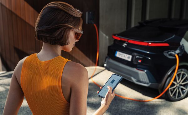 Kobieta korzysta z telefonu podczas ładowania Toyoty ze stacji domowej.