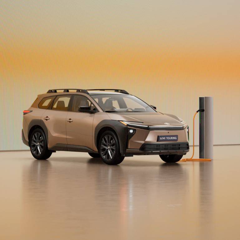 Ein bronzefarbener Toyota bZ4X Touring lädt an einer modernen Wallbox in einem hellen Studio mit warmem Farbverlauf im Hintergrund.