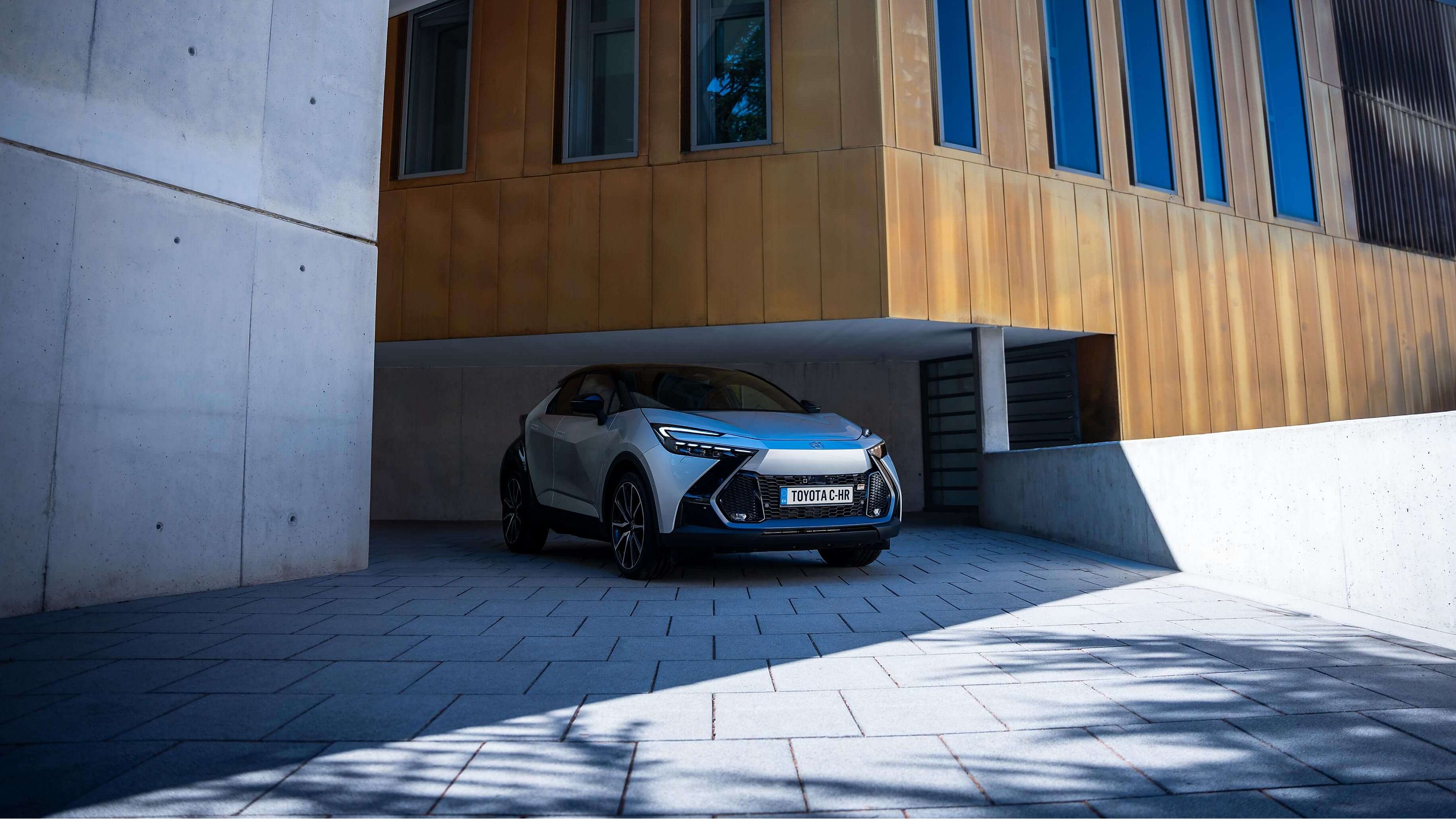Frontansicht eines silbernen Toyota C-HR, geparkt vor einem modernen Gebäude 
