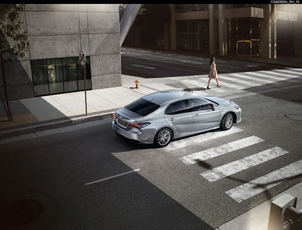 Eine silberne Limousine fährt sanft über eine Stadtstraße und nähert sich einem Zebrastreifen, über den ein Fußgänger geht