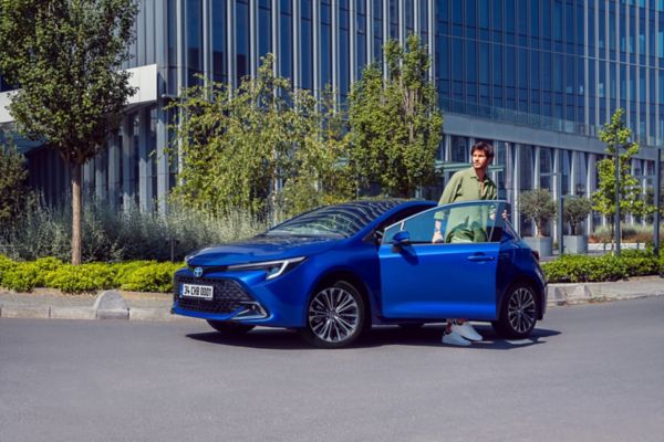 yolda duran mavi Corolla Hatchback Hybrid araç kapısının yanında duran  bir adam