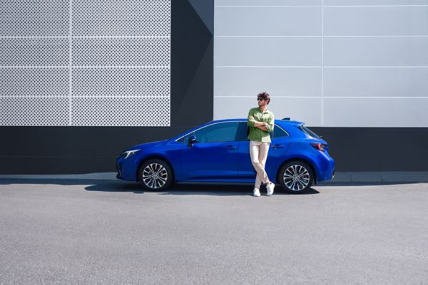 mavi Corolla Hatchback Hybrid araç yanında duran kollarını bağlamış bir adam