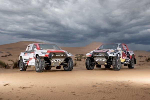 Static front 3/4 shots of two Hilux racing models in the desert