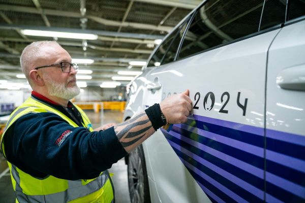 A Toyota manufacturing UK employee with a yellow jacket applying the sticker of Paris 2024 on a white Toyota Corolla door