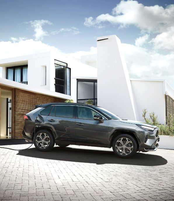 Toyota RAV4 Plug-in Hybrid stoi przed posesją podczas ładowania ze stacji domowej.