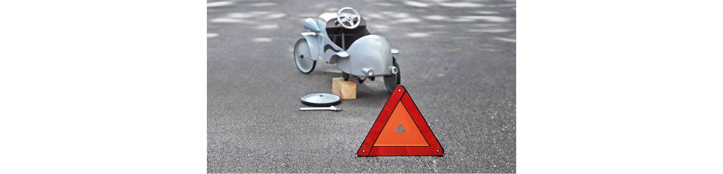 Ein aufgebocktes Kinderfahrzeug mit abmontiertem Rad steht auf einer Straße, im Vordergrund ist ein rotes Warndreieck platziert.