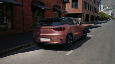 Ein kupferfarbener Lexus LBX steht geparkt im Halbschatten vor einem Gebäude