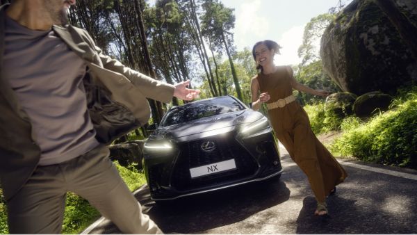 2 people walking in front of a Lexus NX