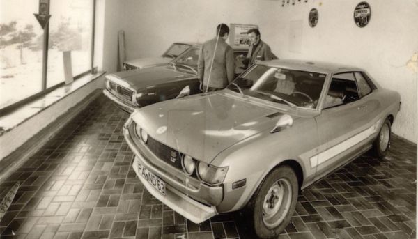 Schwarzweiß-Bild von zwei alten Toyotas und zwei Personen dazwischen