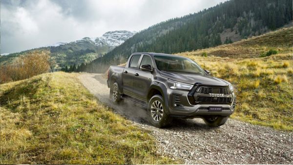 Brauner Pick-up Truck fährt eine steinige Straße entlang. Im Hintergrund ist ein schneebedeckter Berggipfel zu sehen.