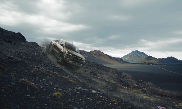 Ein grauer Hilux fährt einen steilen Berg herunter, während im Hintergrund hohe Berge und eine zerklüftete Landschaft zu sehen sind