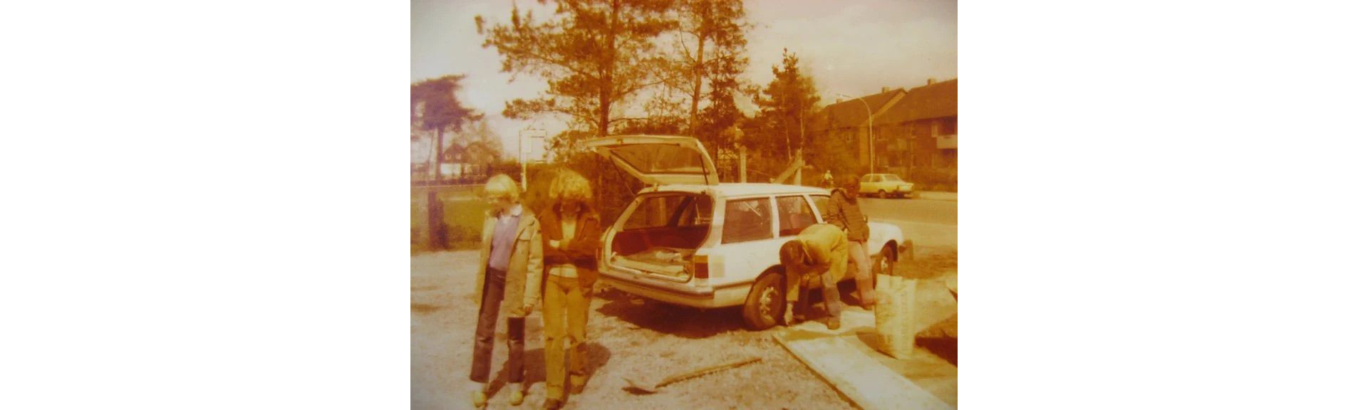 Ein altes Bild von zwei Personen die hinter einem Fahrzeug stehen, während Mechaniker an dem Fahrzeug arbeiten
