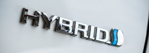 Die Nahaufnahme zeigt das Emblem eines Hybridfahrzeugs als Hinweis auf den alternativen Antrieb.