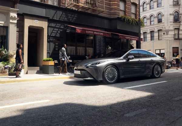 Grauer Toyota Mirai fährt durch die Innenstadt einer Metropole an Hochhäusern vorbei.