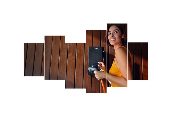 Eine Frau mit kurzen braunen Haaren und einem leuchtend gelben Oberteil lächelt, während sie vor einer Wallbox steht mit einem Ladekabel in der Hand.