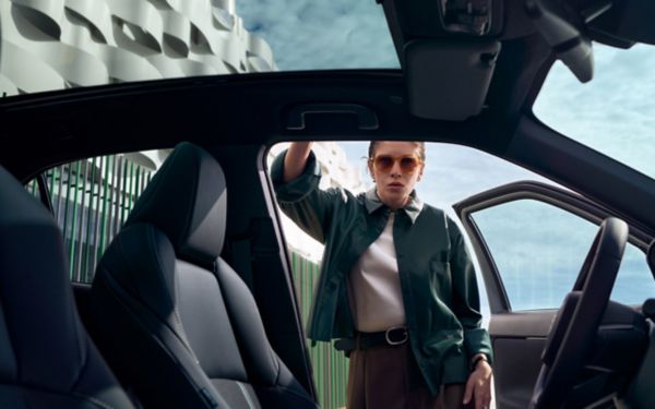 Sicht vom Innenraum eines Fahrzeugs auf die geöffnete Fahrertür, an die sich eine Person mit Sonnenbrille anlehnt.