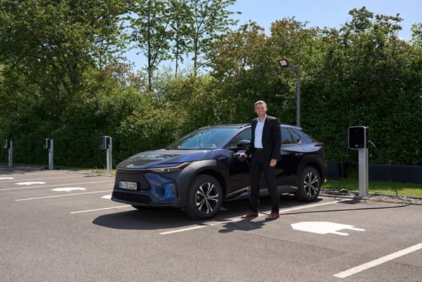 André Schmidt, Präsident der Toyota Deutschland GmbH, steckt einen Ladestecker in einen an einer Ladesäule geparkten Toyota bZ4X.