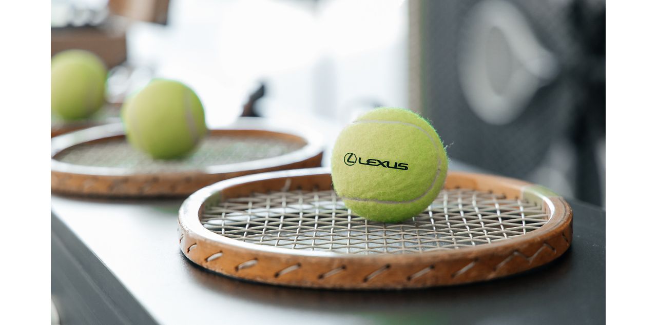 A tennis ball with the Lexus logo on, sat on a tennis racket