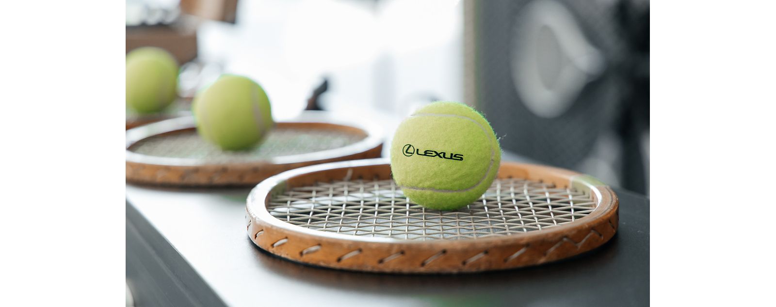 A tennis ball with the Lexus logo on, sat on a tennis racket