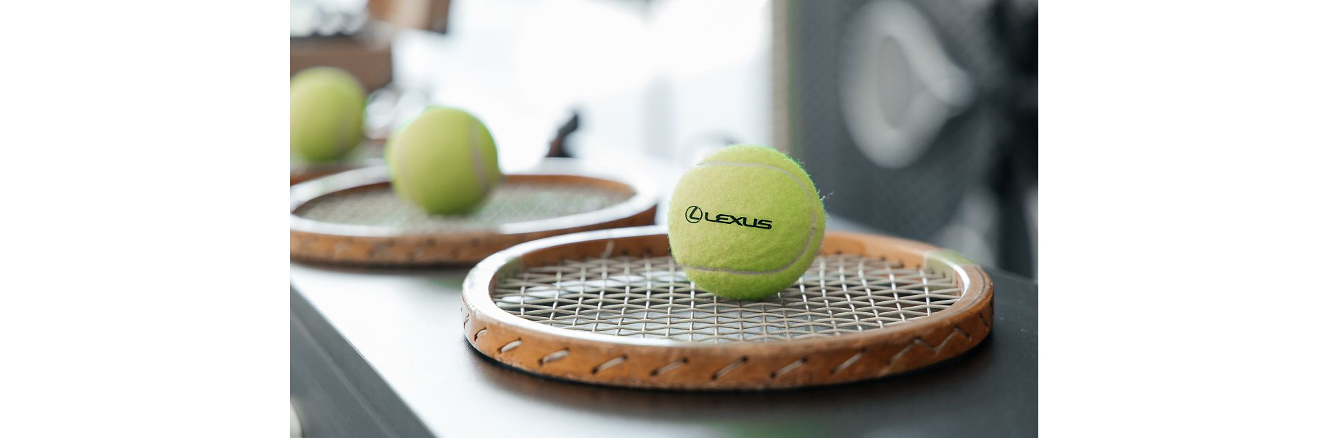 A tennis ball with the Lexus logo on, sat on a tennis racket