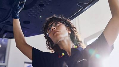 Service-Mitarbeiterin prüft Fahrzeug von unten in einer Werkstatt.