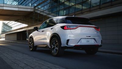 Weißer Lexus LBX fährt durch moderne Stadtarchitektur, Heckansicht.