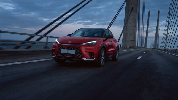 Ein roter Lexus LBX fährt vor einem Abendhimmel über eine Brücke