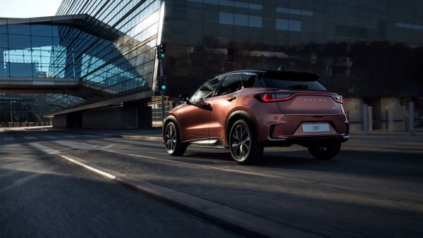 Ein eleganter, moderner Lexus LBX fährt durch eine Stadtstraße, mit reflektierenden Glasgebäuden und einer grünen Ampel im Blick.