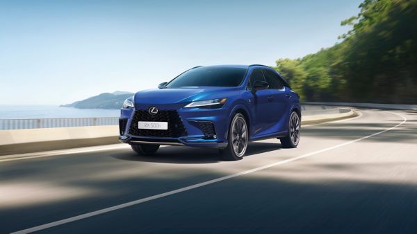 Ein blauer Lexus RX fährt auf einer malerischen Straße am Meer entlang