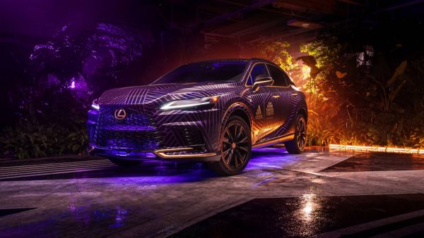 Ein eleganter Lexus-Geländewagen mit einer auffälligen lila-schwarz gemusterten Verkleidung, beleuchtet von bunten Lichtern und umgeben von üppigem Laub.