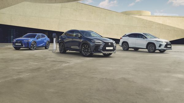 Drei Lexus SUVs nebeneinander vor einem modernen Gebäude geparkt. Der schwarze Geländewagen ist an eine Ladestation angeschlossen, während der weiße und der blaue Geländewagen von hinten zu sehen sind.