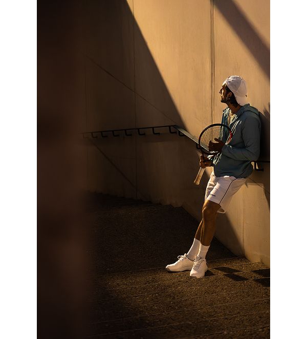 Ein Tennisspieler lehnt im Halbschatten an einer Wand