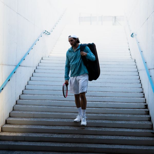 Eine Person im Tennisoutfit und mit Schläger in der Hand steht auf einer Treppe