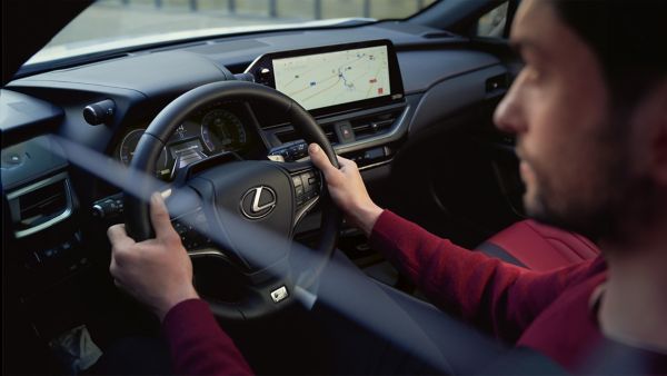 Eine Person am Steuer eines Lexus, die sich auf die Straße konzentriert, während ein GPS-Navigationsbildschirm eine Karte im Armaturenbrett anzeigt.