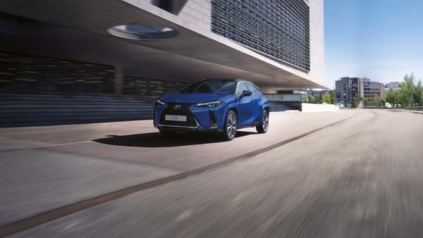 Ein blauer Lexus UX fährt an einem Gebäude entlang