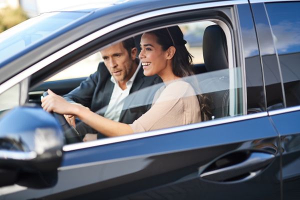 Zwei Personen sitzen in einem Lexus während eine Person der anderen etwas im Auto erklärt
