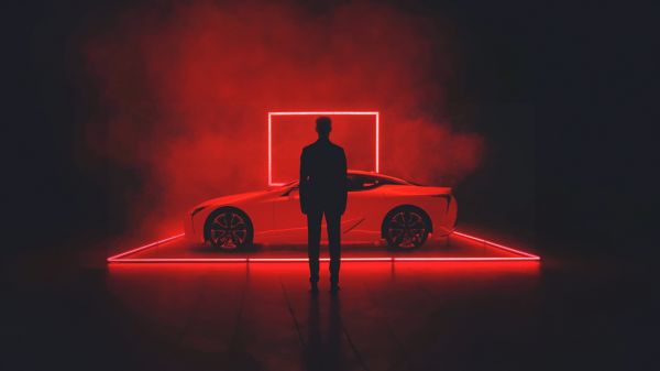 Eine Person steht vor einem in dramatischem Rot beleuchteten Lexus LC
