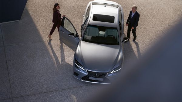 A woman and man walking towards a parked Lexus LS