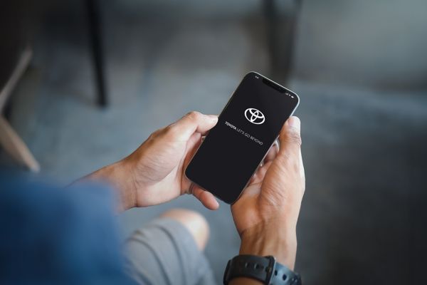 Mężczyzna trzyma w ręku smartfona. Na telefonie pojawi się logo TOYOTA.