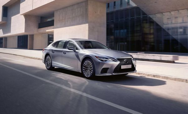 Ein silberner Lexus LS fährt durch eine moderne Stadt
