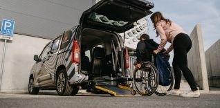 Žena pomáhá muži na invalidním vozíku nastoupit do automobilu.