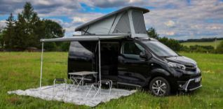 Černá dodávka s markýzou a střešním stanem na louce.