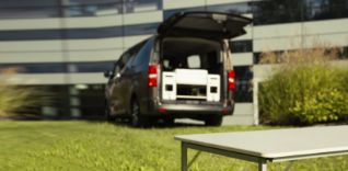 Hnědá dodávka s otevřenými zadními dveřmi a skládacím stolem před ní.