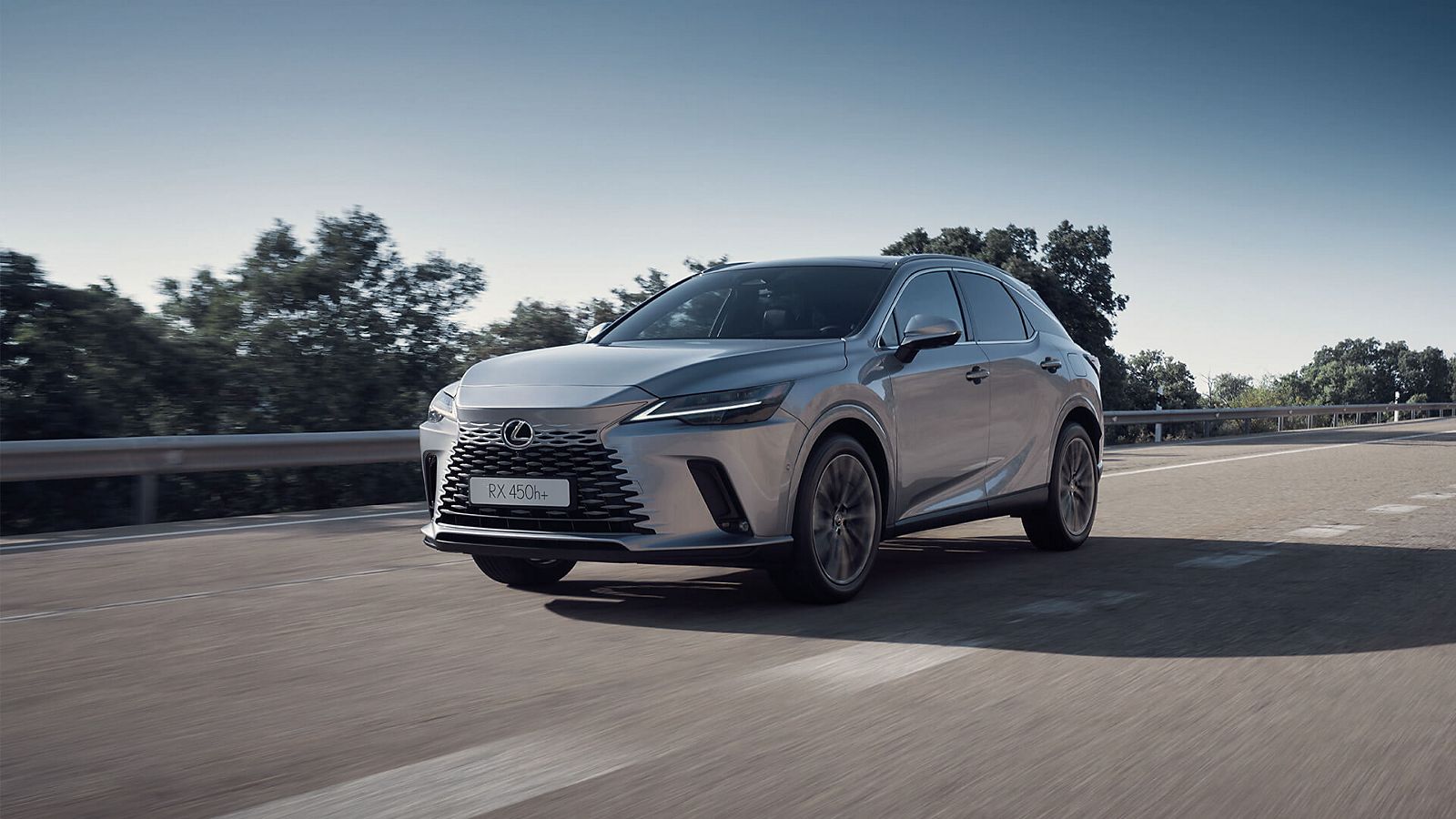Ein Lexus RX fährt über eine Landstraße, die sich durch eine weite, grüne Landschaft schlängelt