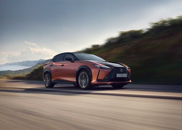 Ein kupferfarbener Lexus RZ fährt eine Landstraße entlang