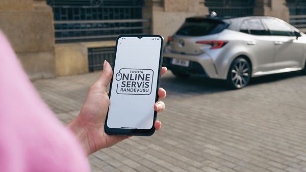 Ekranında "Online servis randevusu" yazan akıllı telefon tutan bir kullanıcı ve Toyota araç