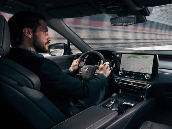 Ein Mann in einem eleganten schwarzen Anzug fährt einen Lexus und konzentriert sich auf die Straße vor ihm. 