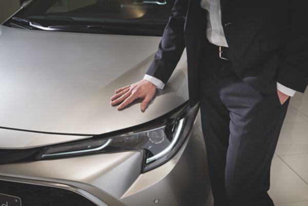 Nahaufnahme eines Geschäftsmann im Anzug, der seine Hand auf die Motorhaube eines silbernen Autos legt