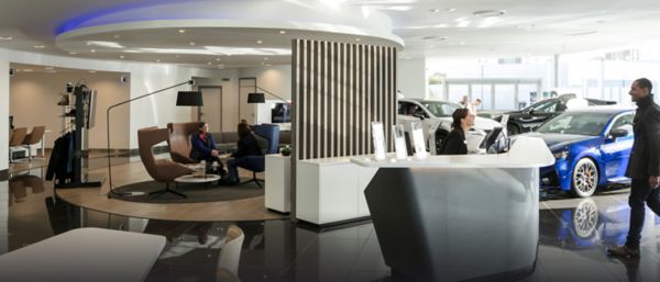 Modernes Lexus Autohaus mit einem Empfangsbereich, Sitzgelegenheiten für Kunden und ausgestellten Fahrzeugen. Zwei Frauen unterhalten sich im Sitzbereich.